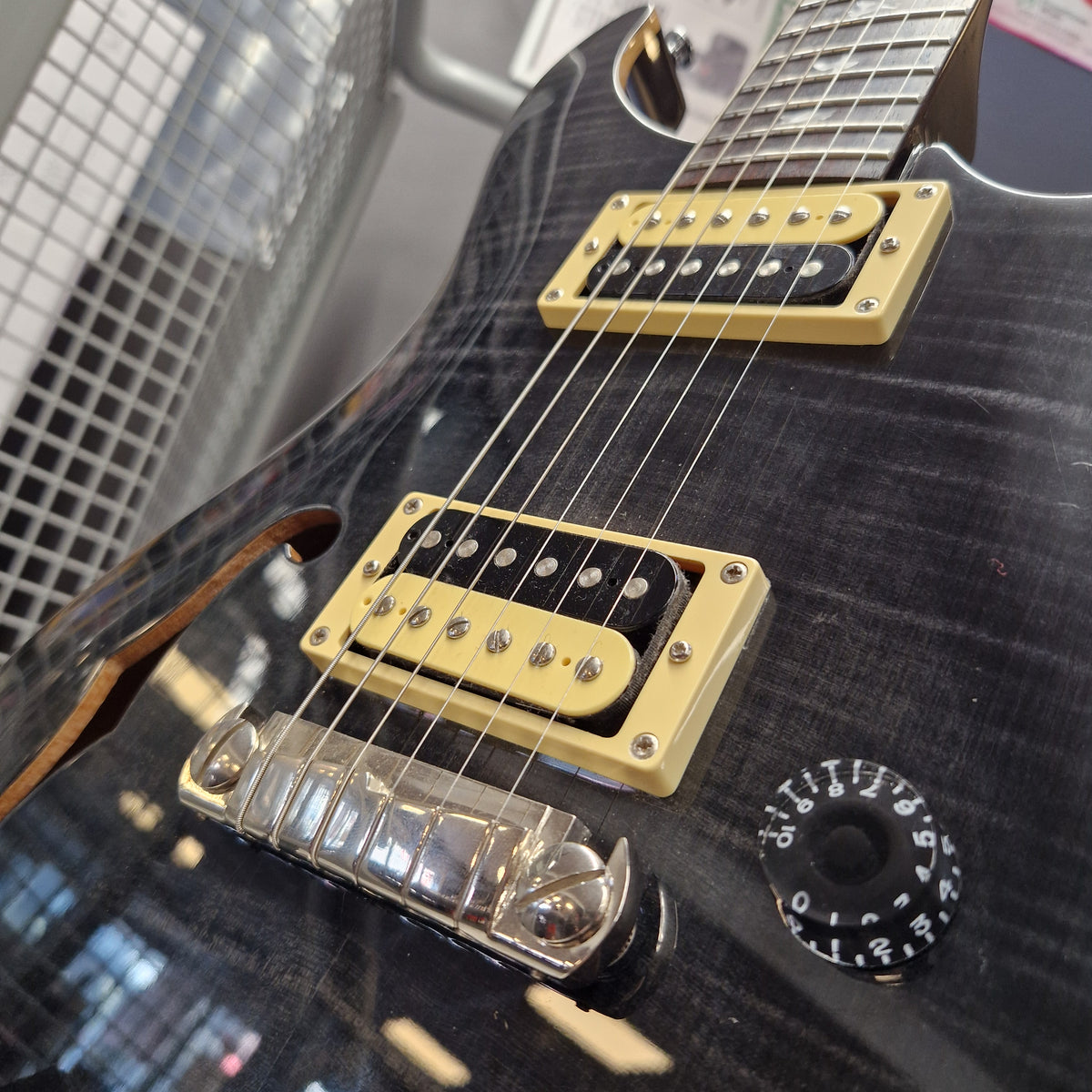 Pre-Owned PRS SE Custom 22 Semi-Hollow Electric Korean - Grey Black Close-up of a black electric guitar body with gold humbucker pickups, a black control knob, and a chrome bridge, photographed indoors with reflections on the glossy finish.