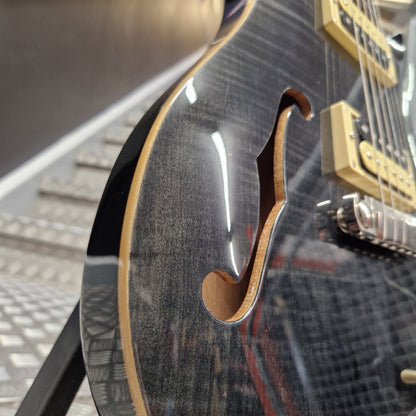 Pre-Owned PRS SE Custom 22 Semi-Hollow Electric Korean - Grey Black Close-up of a black electric guitar body featuring a glossy flamed maple top, a f-hole cutout, and gold-toned pickups.