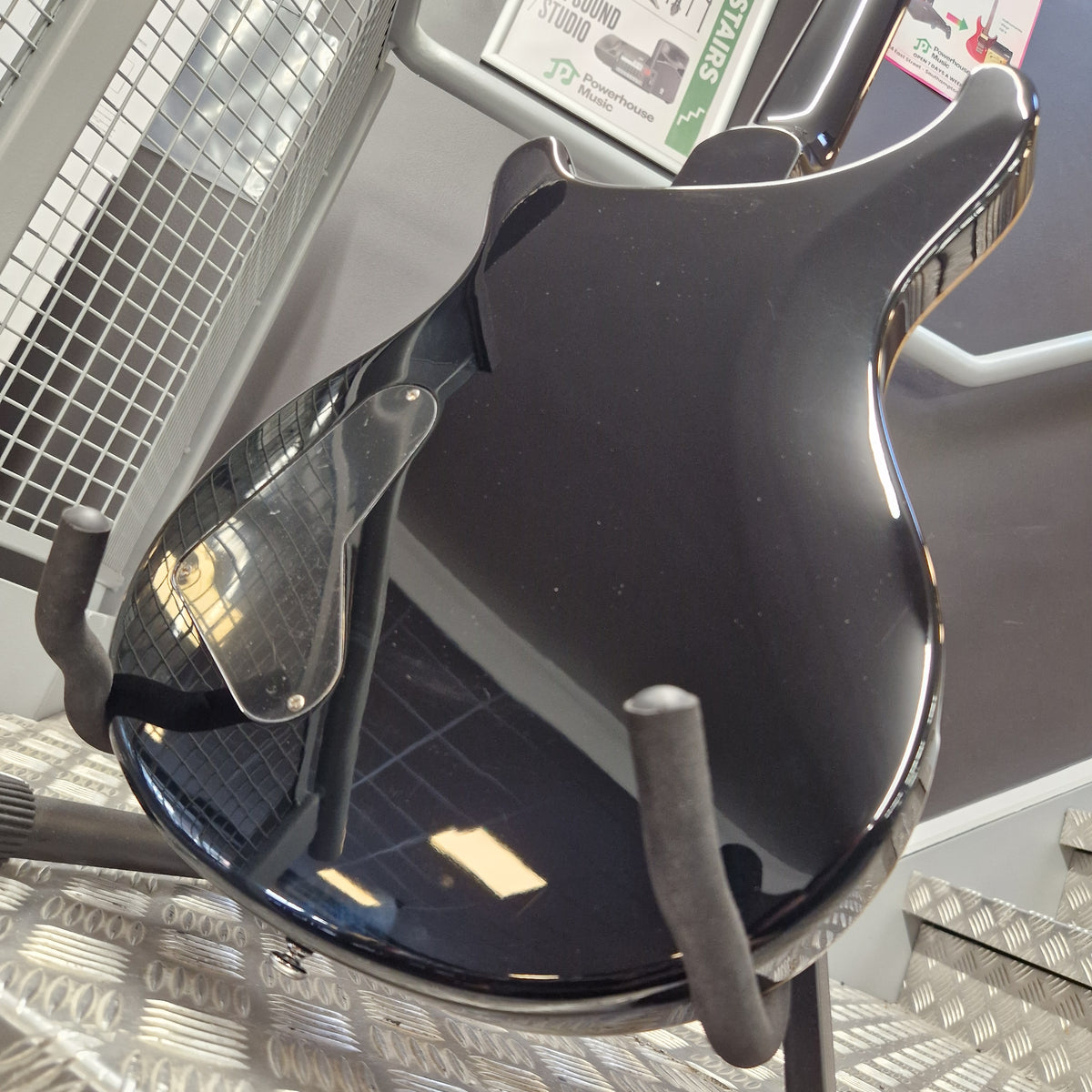Pre-Owned PRS SE Custom 22 Semi-Hollow Electric Korean - Grey Black A glossy black guitar headstock mounted on a display stand inside a store, with metal diamond plate flooring and store fixtures visible in the background.