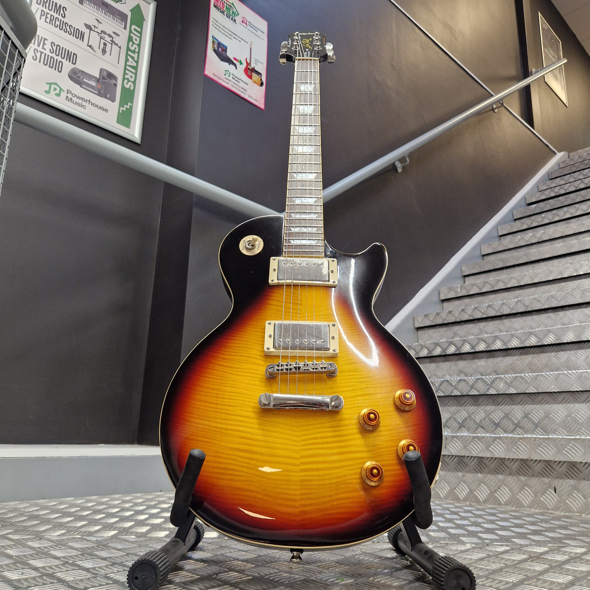 Pre-Owned Epiphone Les Paul Standard Pro Electric - Vintage Sunburst A classic electric guitar with a sunburst finish, displayed on a stand in what appears to be a showroom or garage interior.