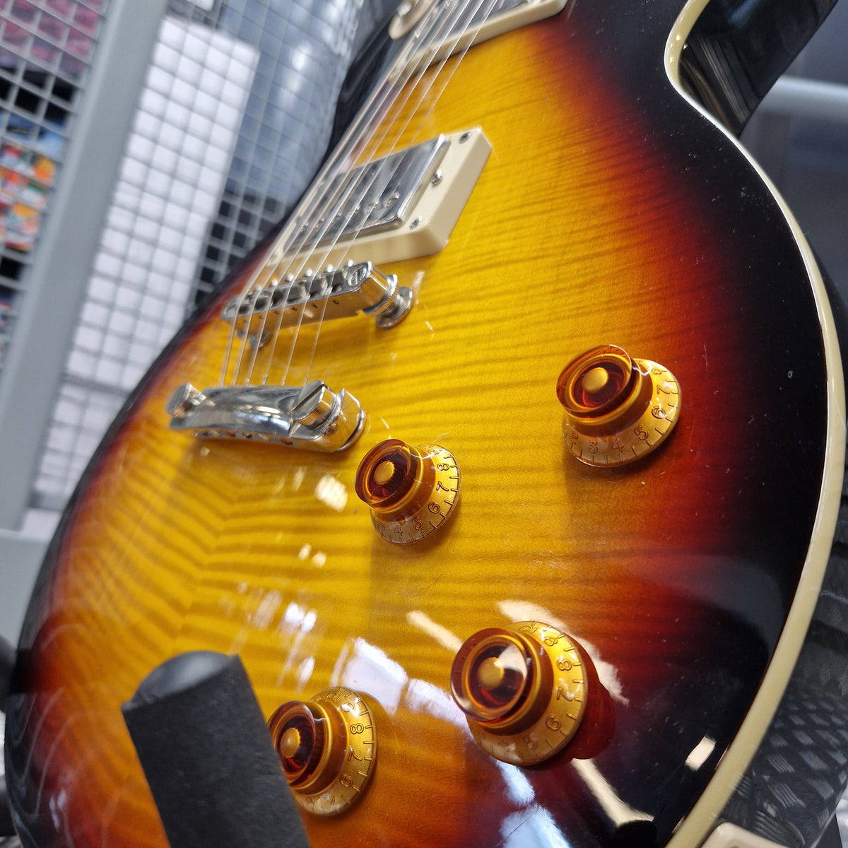 Pre-Owned Epiphone Les Paul Standard Pro Electric - Vintage Sunburst Close-up of a sunburst electric guitar body showing gold-toned control knobs, a cream pickguard, and part of the bridge over a dark gray amplifier.