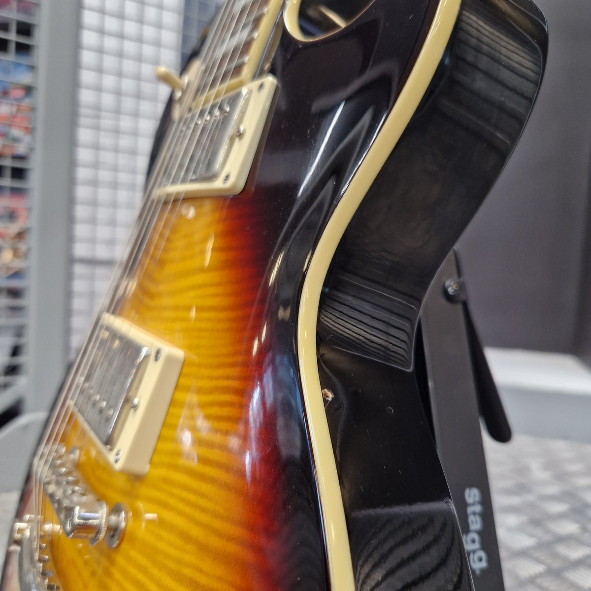 Pre-Owned Epiphone Les Paul Standard Pro Electric - Vintage Sunburst Close-up of the side of a Stagg electric guitar showing a sunburst finish that transitions from black to orange and yellow, with cream-colored hardware and binding.