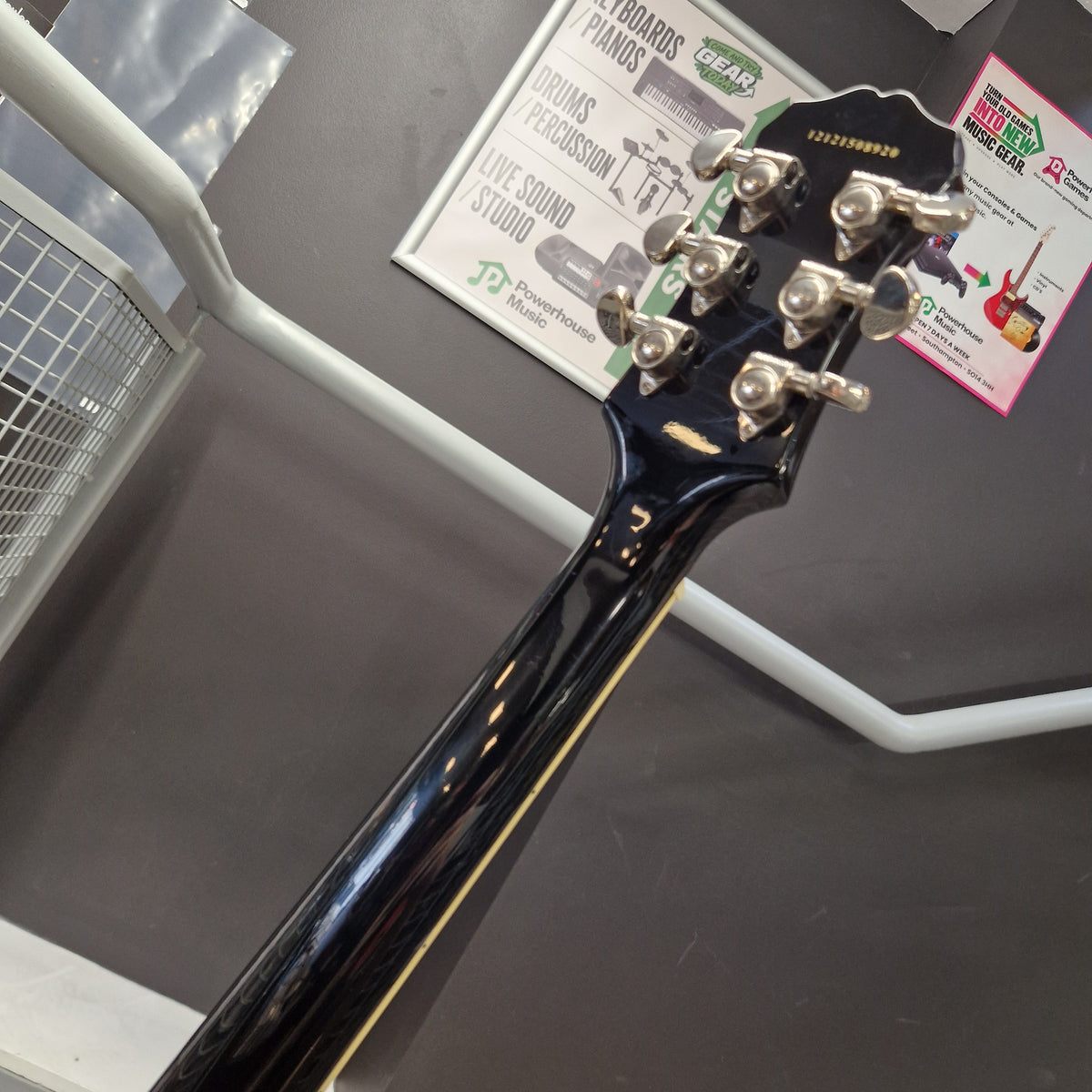 Pre-Owned Epiphone Les Paul Standard Pro Electric - Vintage Sunburst Close-up of the headstock of a glossy black electric guitar, showing six silver tuning pegs and part of the neck, photographed indoors against a dark gray surface with white display brackets.