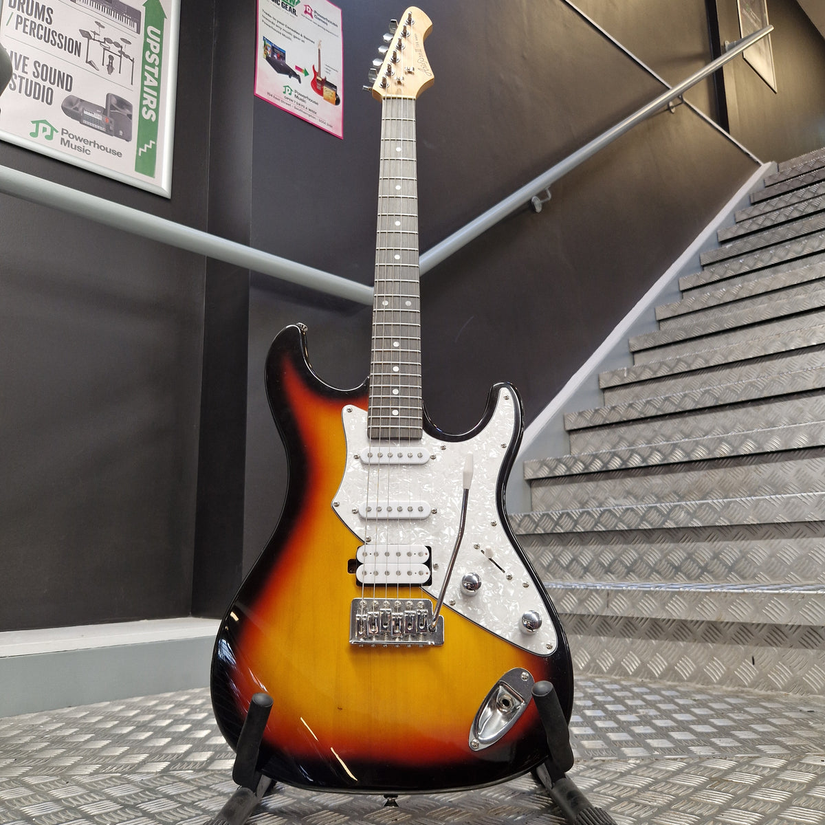 Pre-Owned Aria Pro II 714 Series Electric - Sunburst A classic electric guitar with a sunburst finish, mounted on a display stand in a showroom. The guitar features a white pickguard and chrome hardware, with a headstock partially visible on the left.