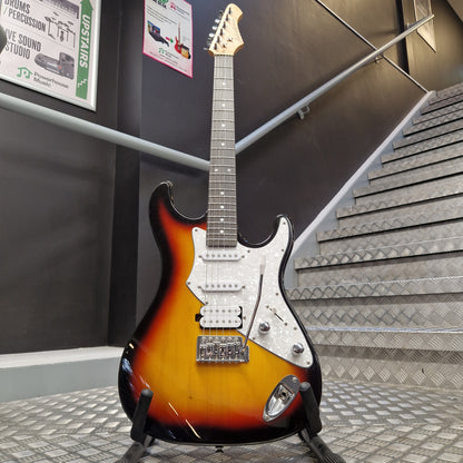 Pre-Owned Aria Pro II 714 Series Electric - Sunburst A classic electric guitar with a sunburst finish, mounted on a display stand in a showroom. The guitar features a white pickguard and chrome hardware, with a headstock partially visible on the left.