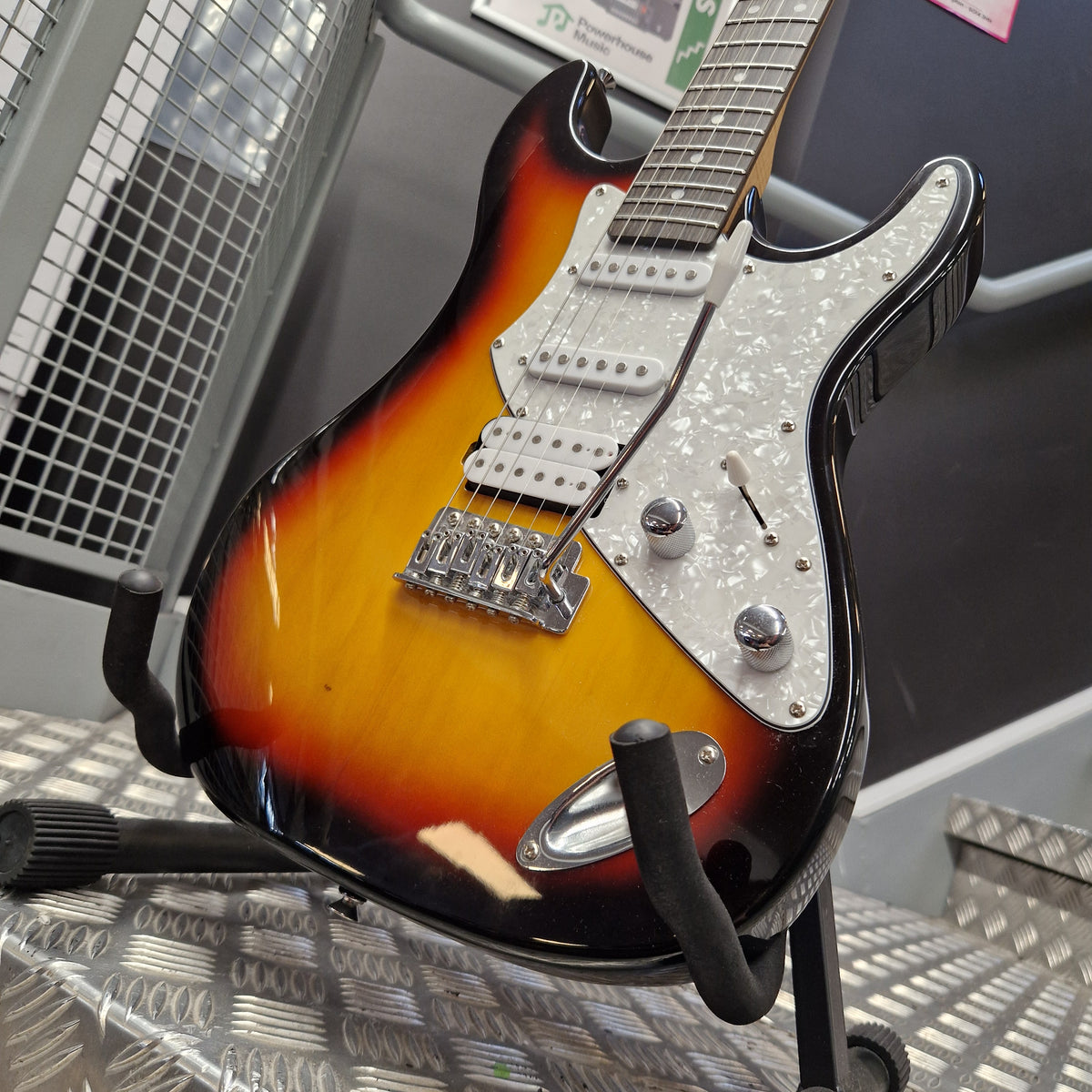 Pre-Owned Aria Pro II 714 Series Electric - Sunburst A close-up of an electric guitar body showing a sunburst finish that transitions from black at the edges to amber-orange in the center, with a white pickguard and chrome hardware.