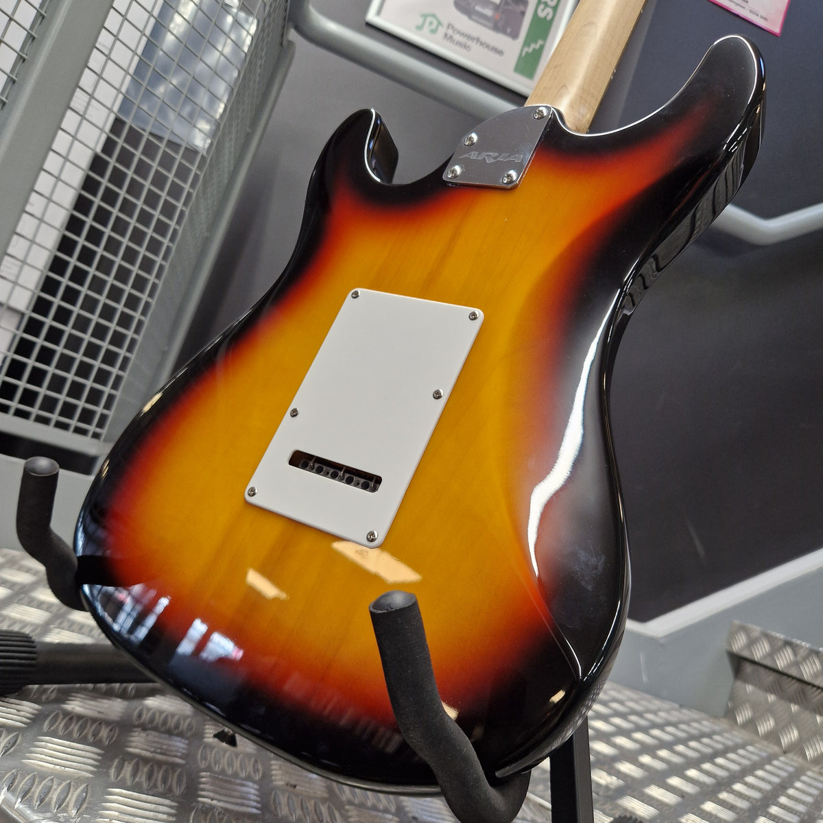 Pre-Owned Aria Pro II 714 Series Electric - Sunburst A close-up of the back of a sunburst electric guitar resting on a stand, showing a glossy orange-to-black finish and a white pickguard.