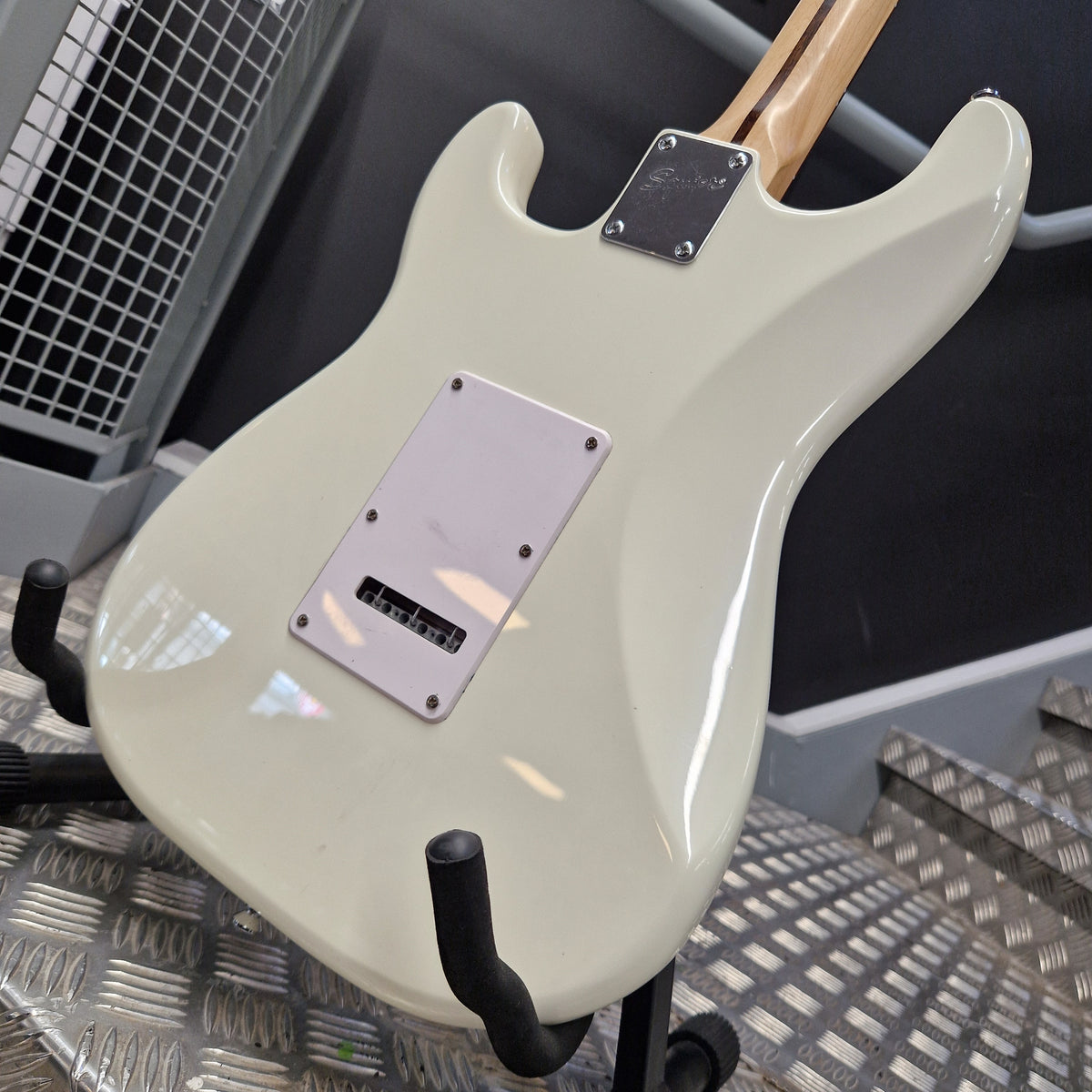 Pre-Owned Squier Bullet Stratocaster Electric - Arctic White The back of an electric guitar with a glossy off-white/cream finish, featuring a silver pickguard and a light wood neck joint, resting on a stand.