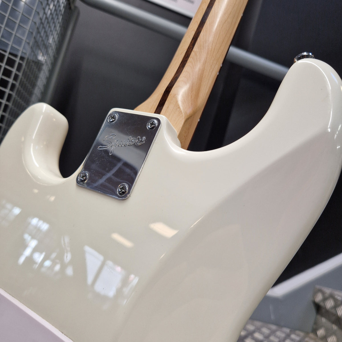Pre-Owned Squier Bullet Stratocaster Electric - Arctic White Close-up of the rear side of an electric guitar body in glossy off-white, showing a chrome hardware plate and part of the natural wood neck.