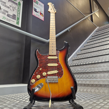 Pre-Owned Jet JS-300 Left-Handed Electric - Sunburst A classic electric guitar with a sunburst finish, mounted on a display wall in what appears to be a showroom or museum. The guitar features a black body with a brown and orange sunburst gradient, a red maple pickguard, and gold-toned hardware.