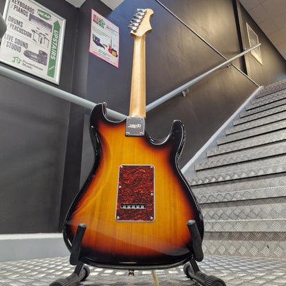 Pre-Owned Jet JS-300 Left-Handed Electric - Sunburst A Fender electric guitar with a classic sunburst finish, hanging on a display stand in a showroom. The guitar features a natural wood neck and a red maple body with a black pickguard and dual humbucker pickups.
