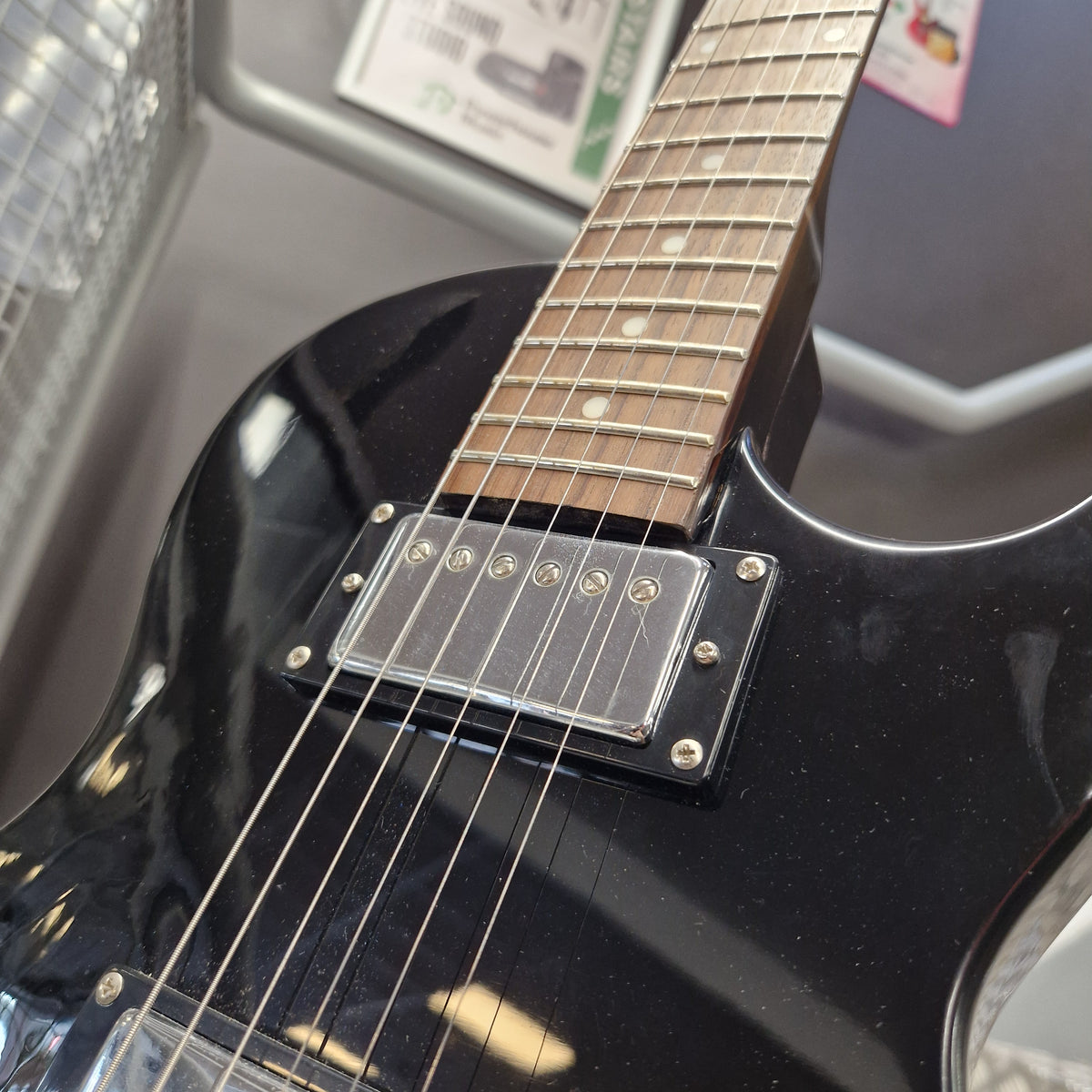 Pre-Owned Marshall MGAP Singlecut Electric - Black Gloss Close-up of a glossy black electric guitar body and part of the fretboard, showing a chrome-covered humbucker pickup and strings.