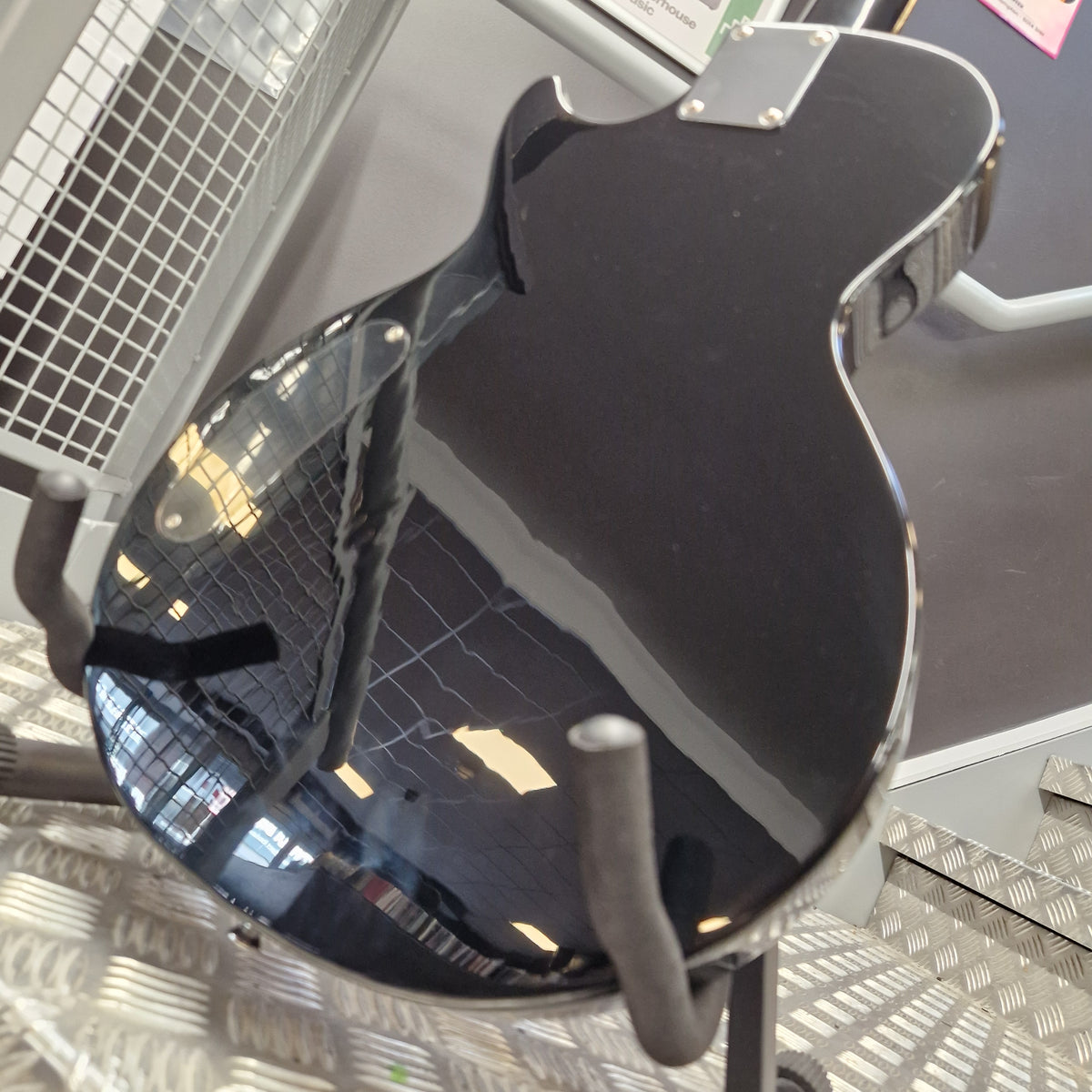 Pre-Owned Marshall MGAP Singlecut Electric - Black Gloss A glossy black electric guitar body shown from a high-angle perspective, resting on a display stand in what appears to be a showroom or shop.