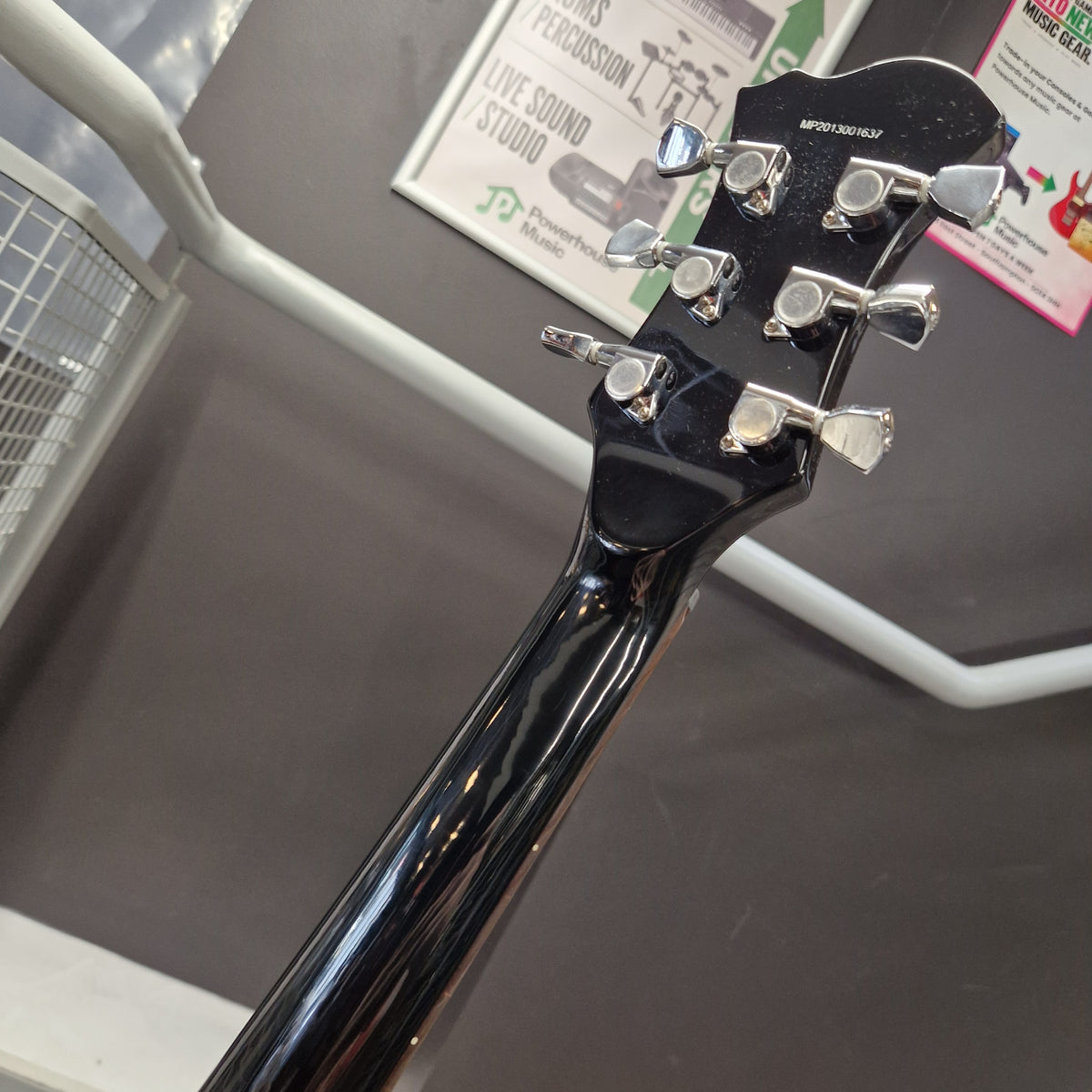 Pre-Owned Marshall MGAP Singlecut Electric - Black Gloss Close-up of the headstock and neck of a glossy black electric guitar, showing six silver tuning pegs and the Gibson logo on the backplate, photographed indoors against a gray wall with store fixtures visible.