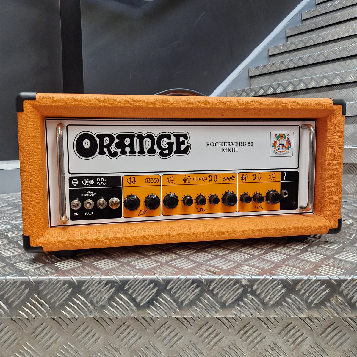 Pre-Owned Orange Rockerverb 50H MKIII Valve Electric Amplifier Head An Orange Rock Miner BS-50 guitar amplifier head in an orange fabric-covered case, photographed from above on a textured silver metal surface.