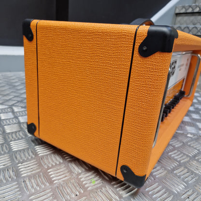 Pre-Owned Orange Rockerverb 50H MKIII Valve Electric Amplifier Head An orange textured guitar amplifier or speaker cabinet with black corner protectors and a metal handle, photographed on a diamond-plate metal surface.