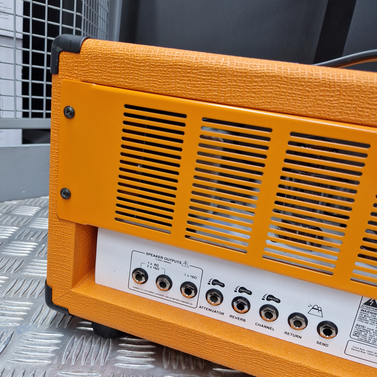 Pre-Owned Orange Rockerverb 50H MKIII Valve Electric Amplifier Head Close-up of the rear panel of an orange guitar amplifier, showing ventilation grilles, control knobs, and a white label on a textured orange cabinet.