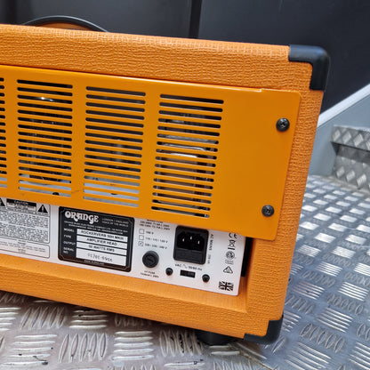 Pre-Owned Orange Rockerverb 50H MKIII Valve Electric Amplifier Head Close-up of the back of an Orange guitar amplifier, showing the orange textured cabinet, vent grille, power input, and control labels, resting on a diamond plate metal surface.