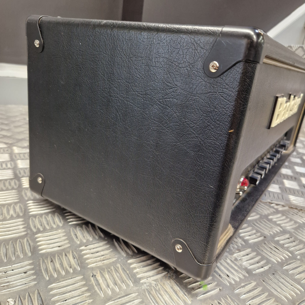 Pre-Owned Blackstar HT Club 50 Electric All-Valve Amplifier Head A black textured leather or vinyl guitar amplifier cabinet shown at an angle, resting on a silver diamond plate metal surface.