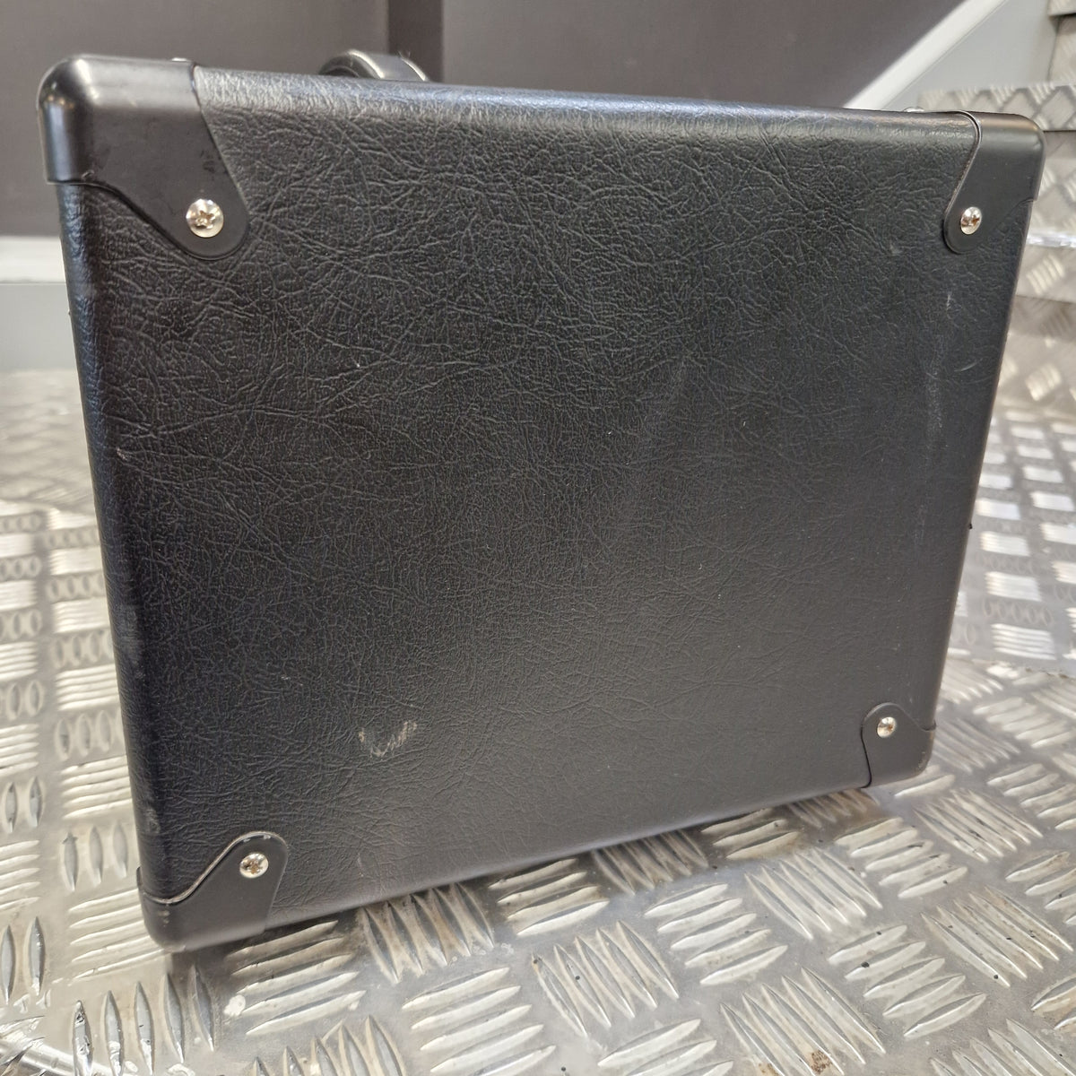Pre-Owned Blackstar HT Club 50 Electric All-Valve Amplifier Head A black textured faux-leather or leather-bound notebook, binder, or case with metal corner rivets, shown from a top-down angle on a silver diamond plate metal surface.