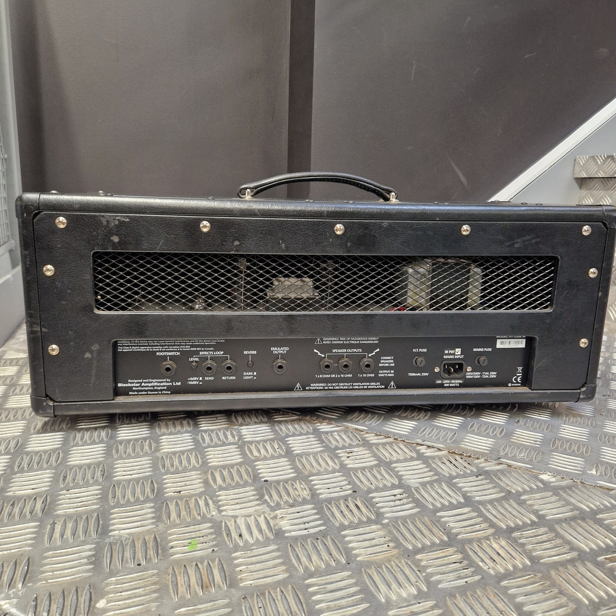 Pre-Owned Blackstar HT Club 50 Electric All-Valve Amplifier Head A black metal guitar amplifier cabinet shown from the back, featuring a mesh grille, screw holes, and multiple input/output jacks, photographed on a diamond plate metal floor.