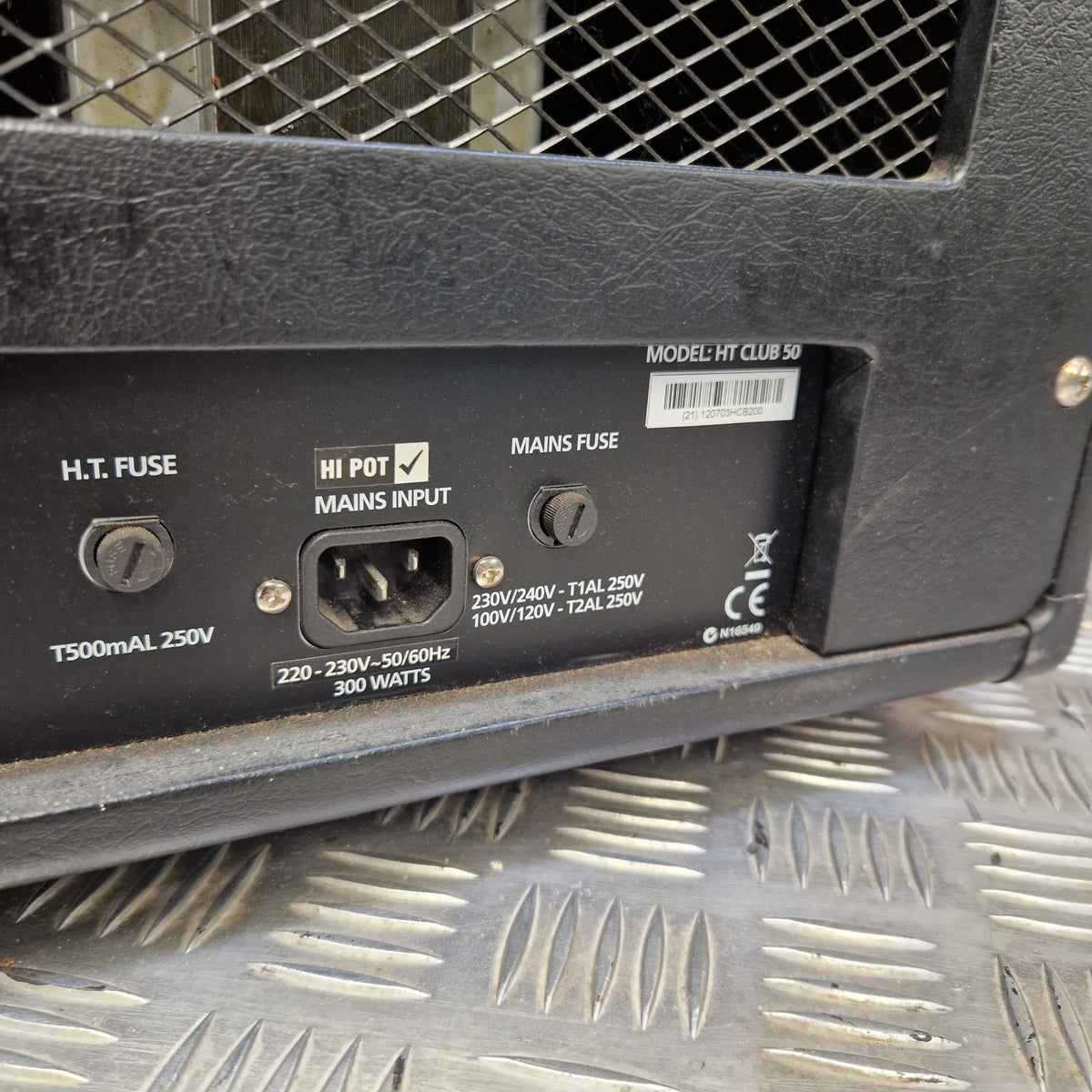 Pre-Owned Blackstar HT Club 50 Electric All-Valve Amplifier Head Close-up of the rear power supply input panel of a black speaker, showing the mains fuse, HT fuse, and mains input socket, photographed on a textured metal surface.