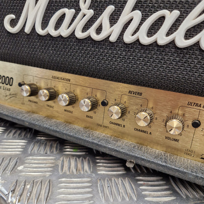 Pre-Owned Marshall JCM2000 DSL100 Valve Electric Amplifier Head Close-up of a Marshall amplifier control panel with metallic knobs and a brushed metal face, next to a textured black speaker grille with white Marshall lettering.
