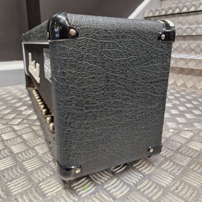 Pre-Owned Marshall JCM2000 DSL100 Valve Electric Amplifier Head A close-up of a black textured guitar speaker cabinet corner with metal corner guards and a visible speaker grille, photographed against a diamond-plate metal background.