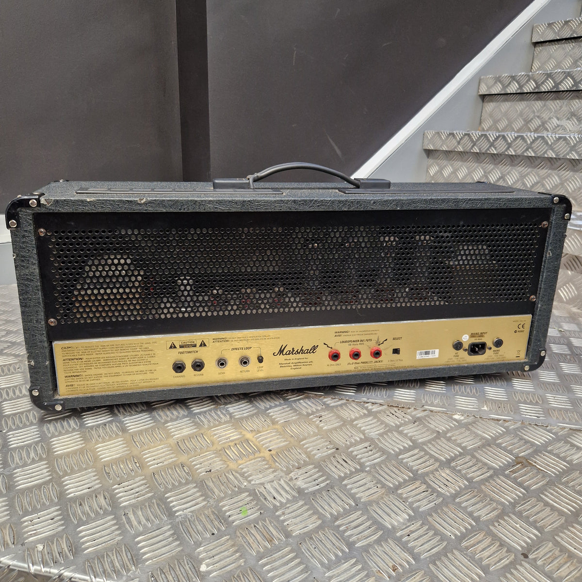 Pre-Owned Marshall JCM2000 DSL100 Valve Electric Amplifier Head A Marshall amplifier head photographed from above on a diamond-plate metal floor next to a staircase.