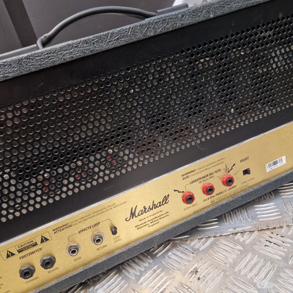 Pre-Owned Marshall JCM2000 DSL100 Valve Electric Amplifier Head Close-up of a Marshall amplifier front panel with a black perforated grille and a gold control panel showing red and black input/output jacks.