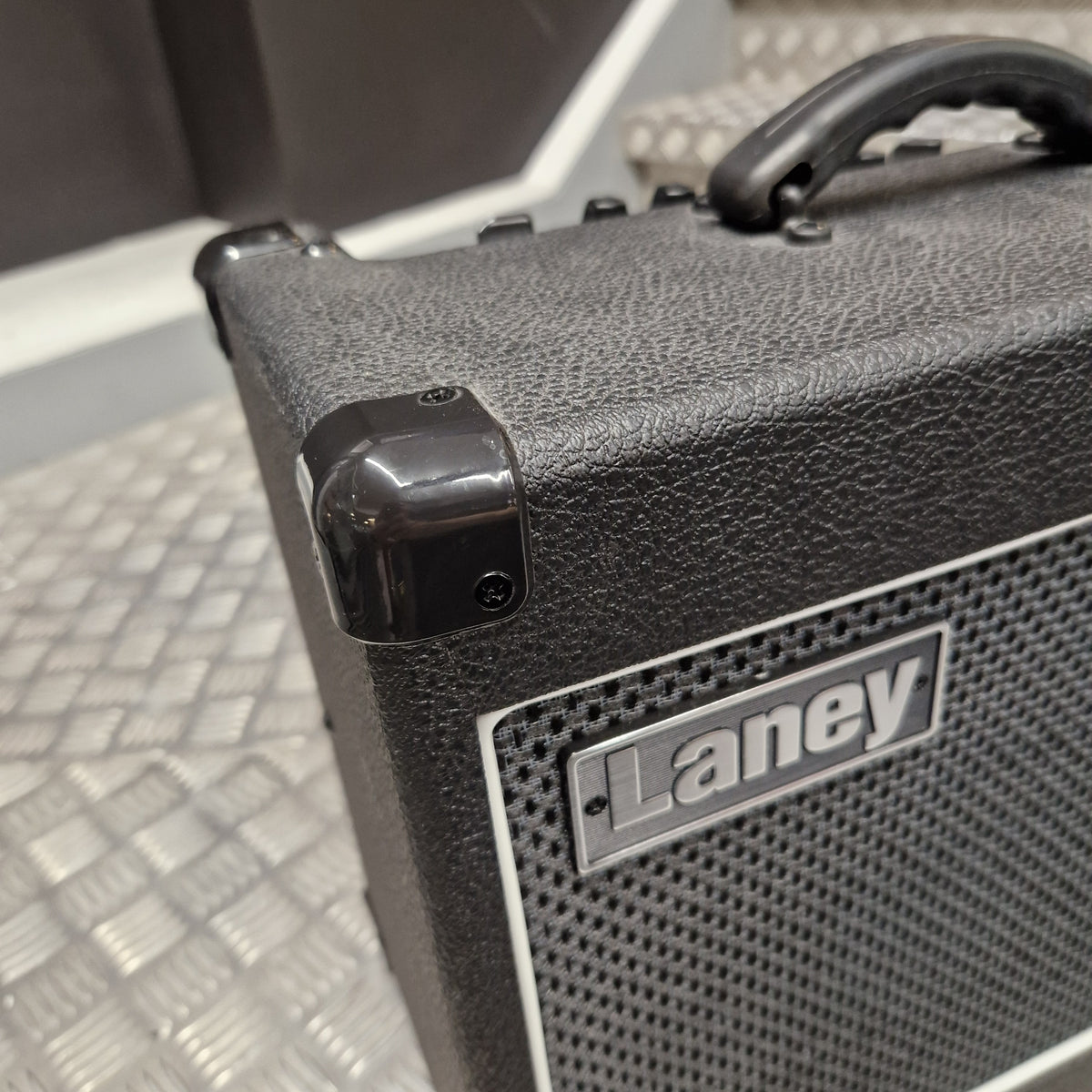 Pre-Owned Laney LG20R 20w Electric Guitar Combo Close-up of a black textured Laney speaker cabinet corner with a glossy black handle and a silver Laney logo badge on a perforated grille.