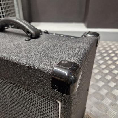 Pre-Owned Laney LG20R 20w Electric Guitar Combo Close-up of a black textured speaker cabinet corner with a glossy black protective cap and a metal mesh grille on a silver metal platform.