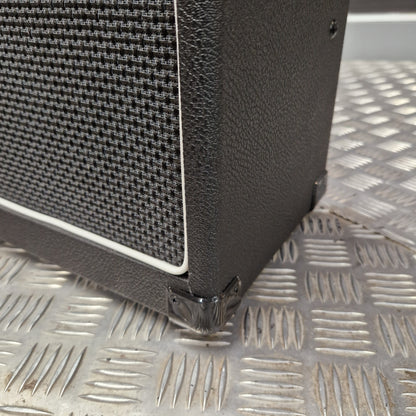 Pre-Owned Laney LG20R 20w Electric Guitar Combo Close-up of a black textured speaker cabinet corner with a black mesh grille and white edge trim, photographed against a silver diamond-plate metal background.