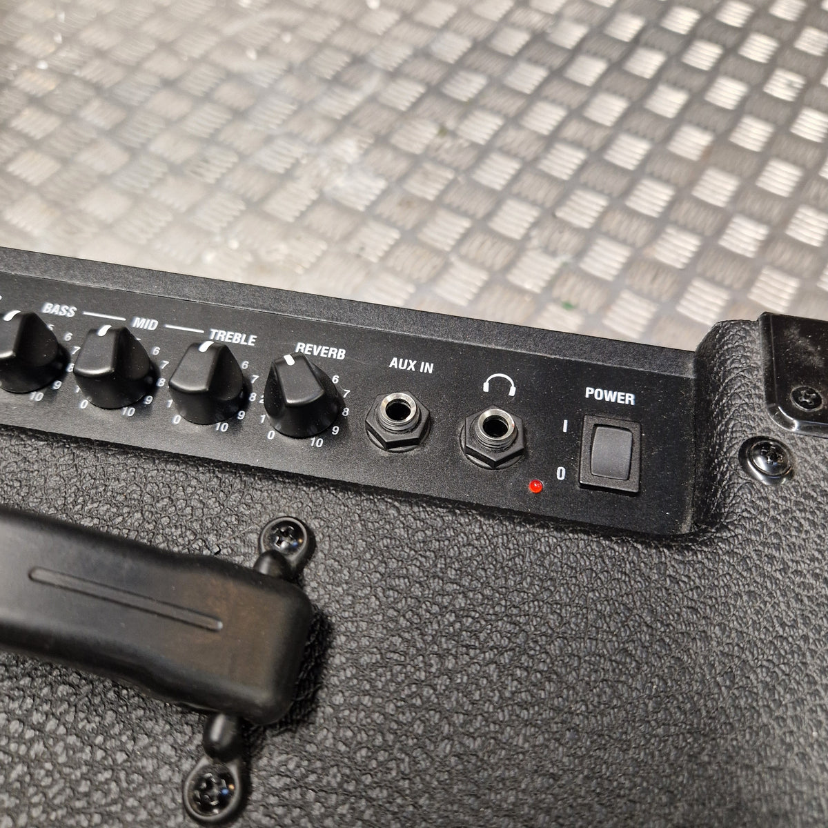 Pre-Owned Laney LG20R 20w Electric Guitar Combo Close-up of a black guitar amplifier control panel with knobs, jacks, and a power switch, resting on a textured black amplifier body with a diamond-plate metal background.