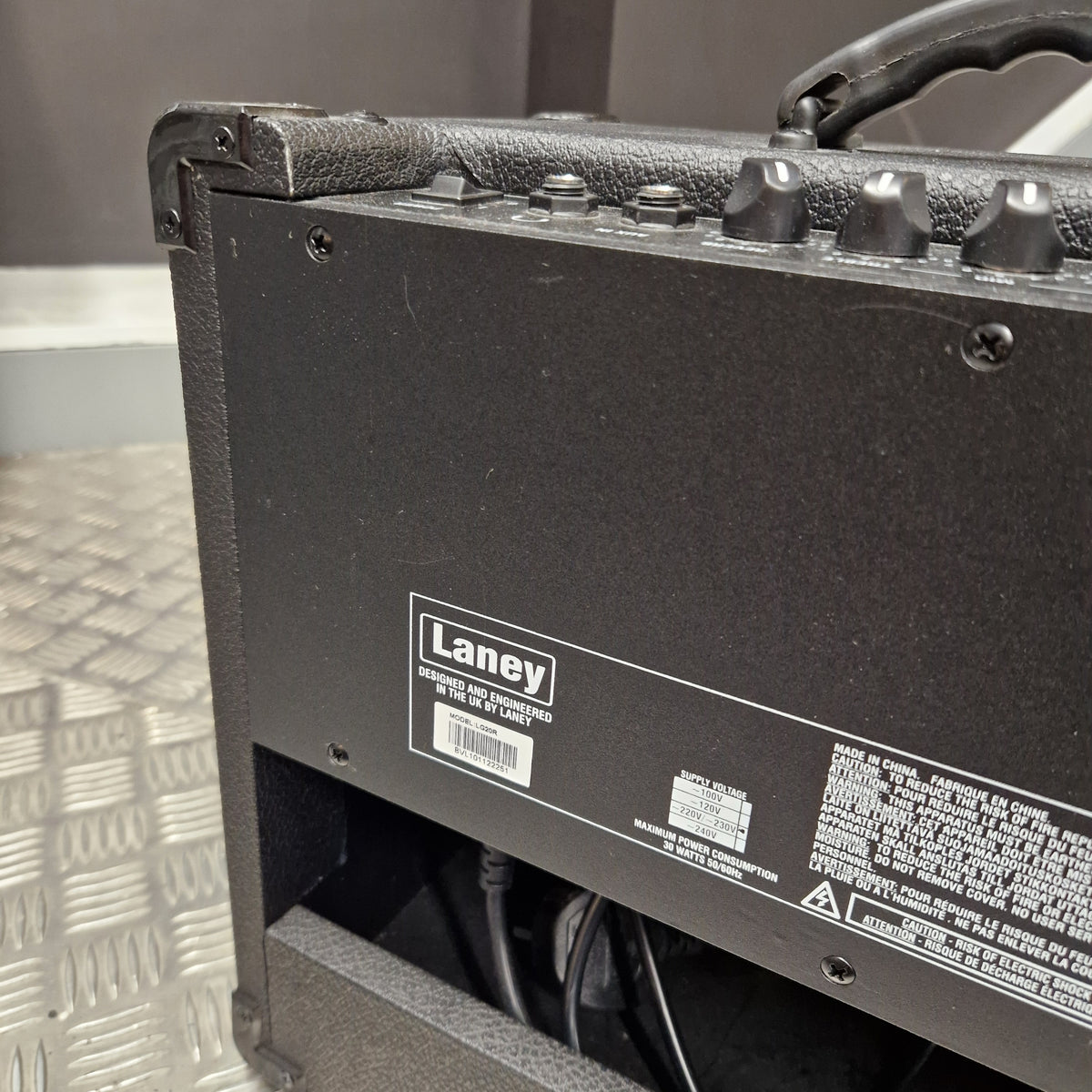 Pre-Owned Laney LG20R 20w Electric Guitar Combo Close-up of the side and back of a black Laney guitar amplifier, showing the model name 'Grit 112' and product information labels on a metal diamond plate floor.