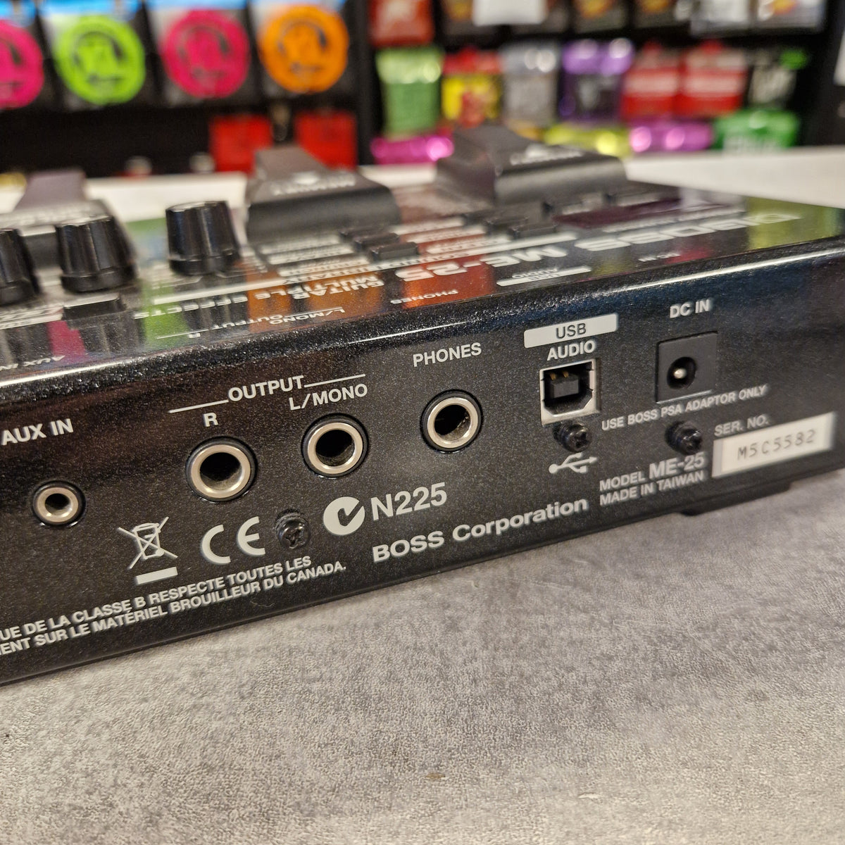 Pre-Owned Boss ME-25 Multi-Effects Pedal Close-up of the rear panel of a Boss N225 audio device, showing input and output jacks, knobs, and branding on a gray surface.