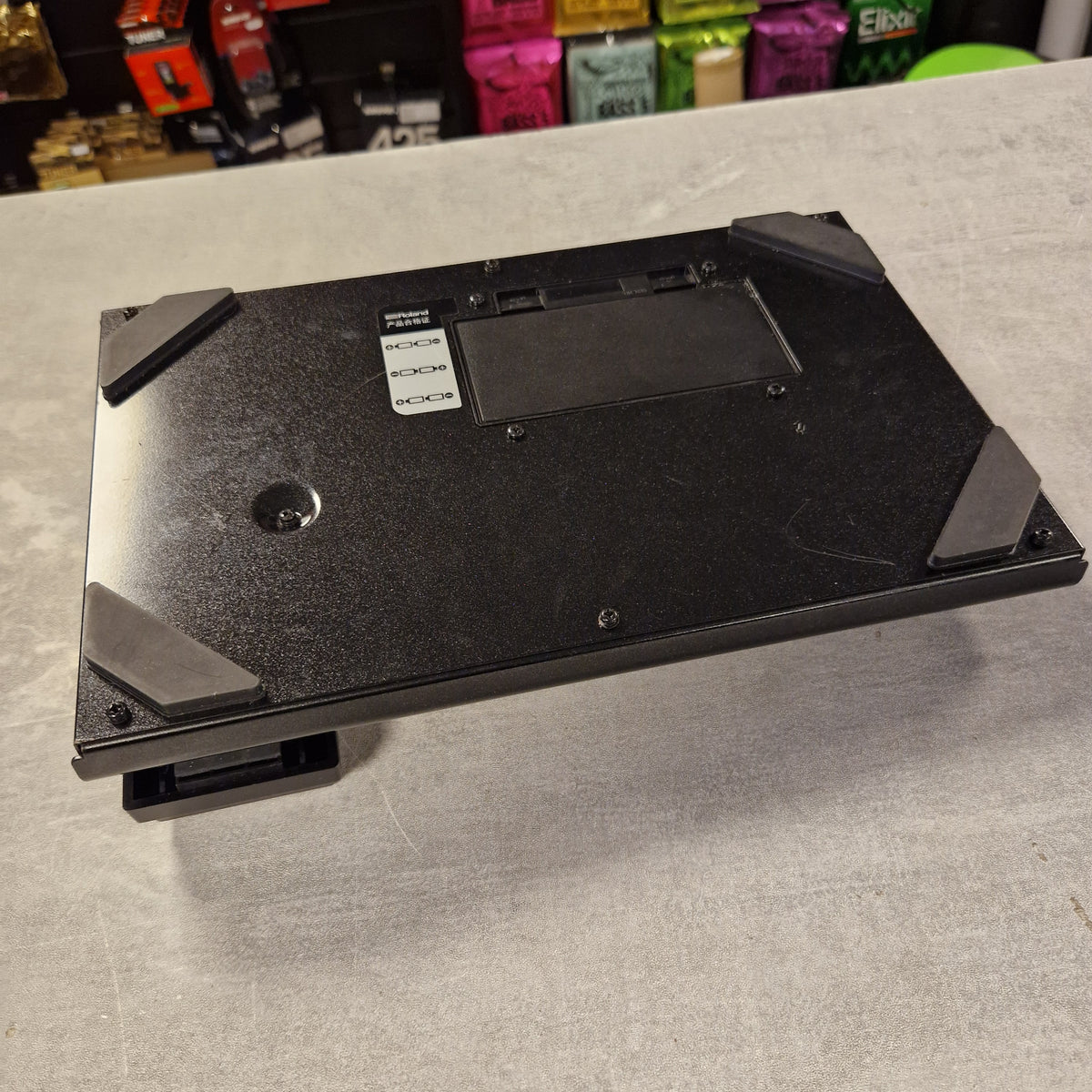 Pre-Owned Boss ME-25 Multi-Effects Pedal The underside of a black gaming keyboard, showing the metal chassis, mounting holes, and protective rubber feet, photographed on a gray textured surface.