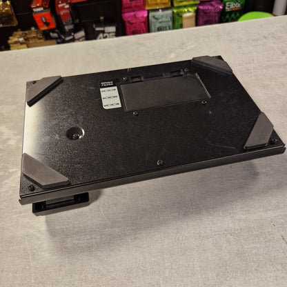 Pre-Owned Boss ME-25 Multi-Effects Pedal The underside of a black gaming keyboard, showing the metal chassis, mounting holes, and protective rubber feet, photographed on a gray textured surface.