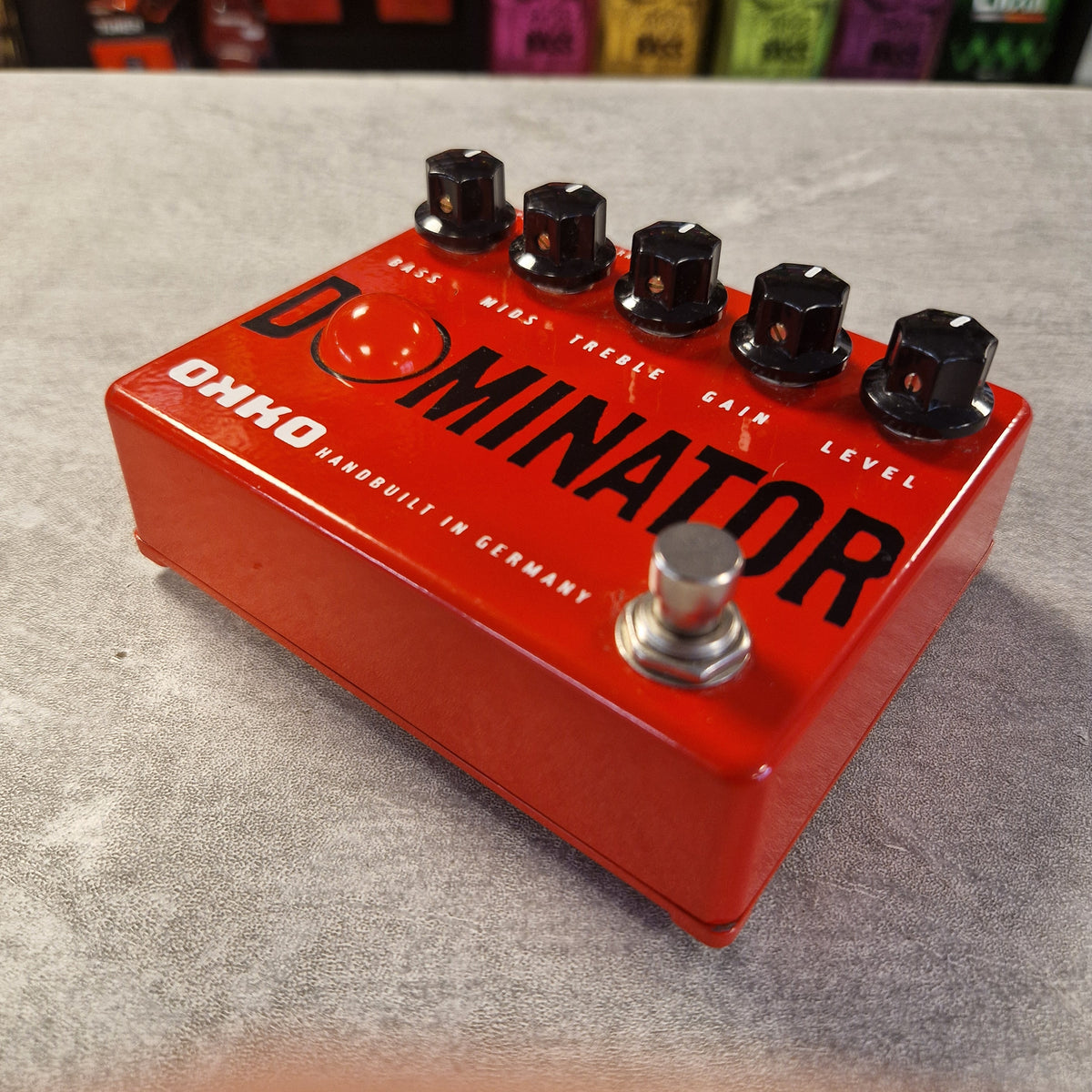 Pre-Owned Okko Dominator High Gain Distortion Pedal - A red Ohio Dominator guitar effects pedal with four black knobs and a silver footswitch, photographed on a gray textured surface.