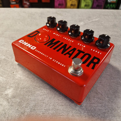 Pre-Owned Okko Dominator High Gain Distortion Pedal - A red Ohio Dominator guitar effects pedal with four black knobs and a silver footswitch, photographed on a gray textured surface.