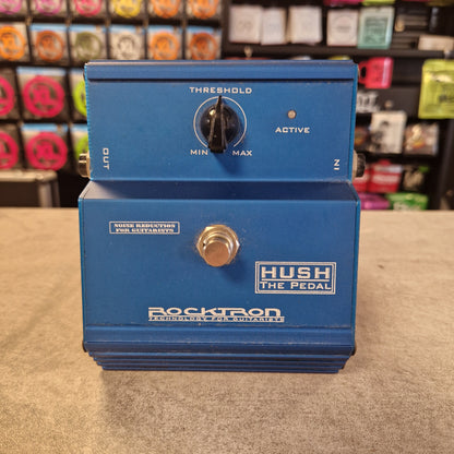 Pre-Owned Rocktron Hush Noisegate Pedal - A blue Rocktron Hush The Pedal guitar effects unit with a footswitch, set on a gray surface with a blurred store background.