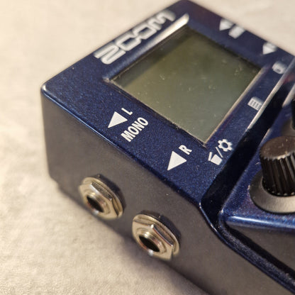 Pre-Owned Zoom MS-100BT MultiStomp Guitar Pedal with Bluetooth - Close-up of a blue ZOOM2 guitar effects pedal with a digital display screen, white control labels, and metal input/output jacks on a light textured surface.