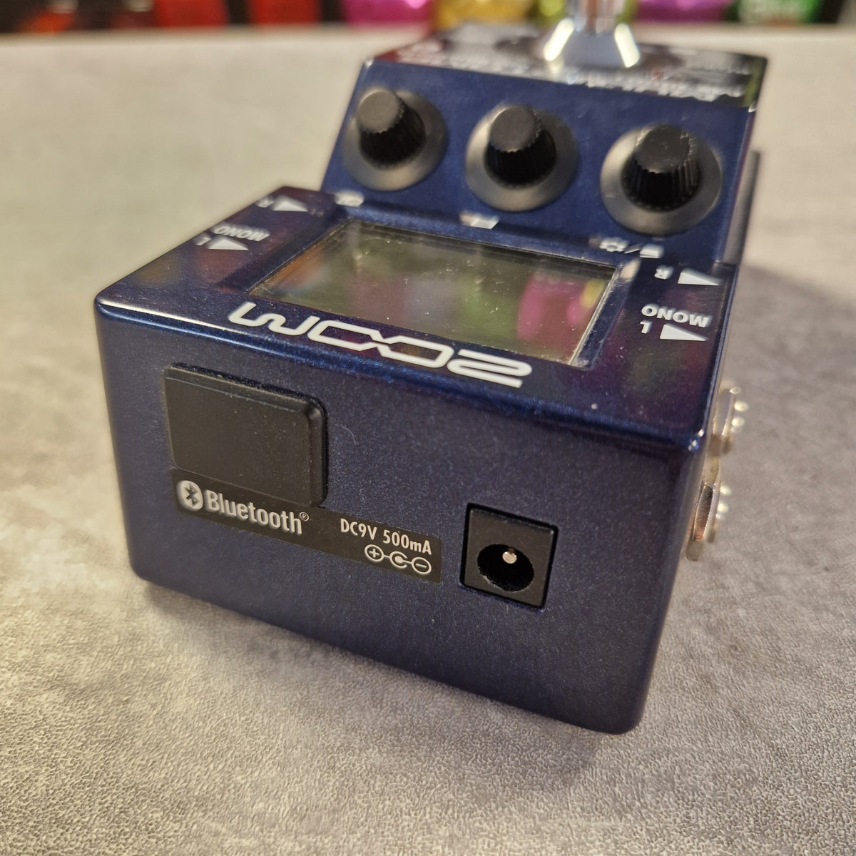Pre-Owned Zoom MS-100BT MultiStomp Guitar Pedal with Bluetooth - A blue Wanda FX2 Bluetooth guitar pedal with three black knobs, a small display screen, and a power input jack, photographed on a gray textured surface.