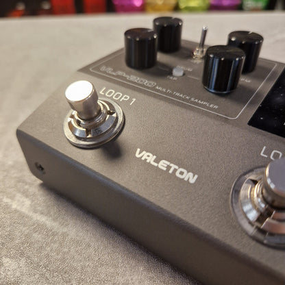 Pre-Owned Valeton VLP-200 Multi-Track Sampler w/ Box - A close-up shot of a Vauleton multi-track sampler pedal, showing the dark gray metal casing, black knobs, and silver footswitches on a textured gray surface.