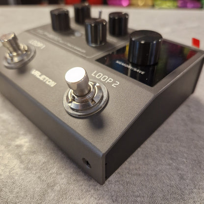 Pre-Owned Valeton VLP-200 Multi-Track Sampler w/ Box - A close-up shot of a Voxeteration Vileton guitar effects pedal, featuring a matte dark gray metal body, black knobs, and silver footswitches on a textured gray surface.
