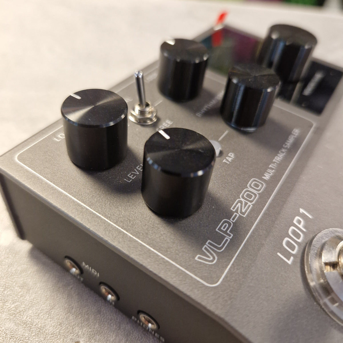 Pre-Owned Valeton VLP-200 Multi-Track Sampler w/ Box - Close-up of a gray VLP-200 multi-track sampler loop pedal with black knobs, a silver toggle switch, and white printed labels on a light gray surface.