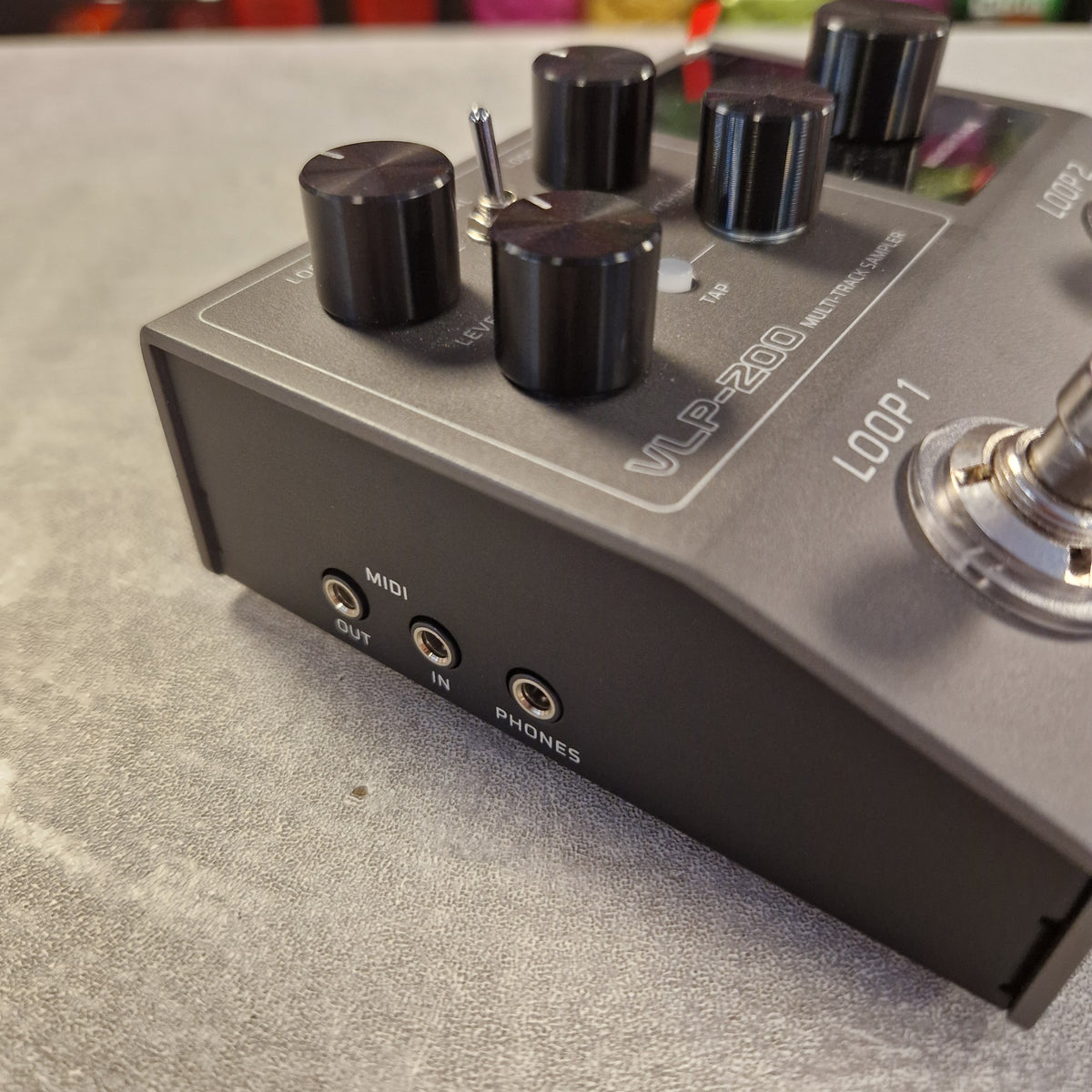 Pre-Owned Valeton VLP-200 Multi-Track Sampler w/ Box - A close-up shot of a VLP-200 multi-effects guitar pedal on a textured gray surface. The pedal has a dark gray metal casing with black knobs, a silver toggle switch, and various input/output jacks including MIDI, IN, PHONES, and LOOP1.
