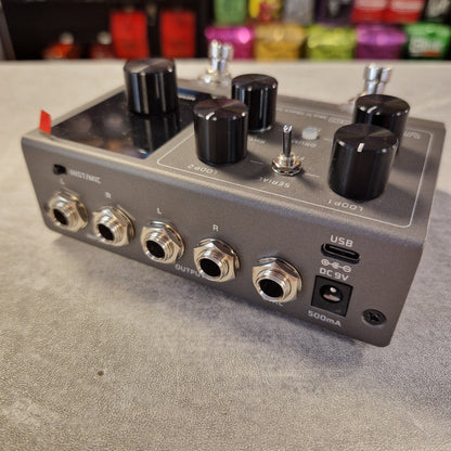 Pre-Owned Valeton VLP-200 Multi-Track Sampler w/ Box - A gray electric guitar effects pedal with black knobs, silver jacks, and a USB-C port, photographed on a gray tabletop with colorful blurred items in the background.