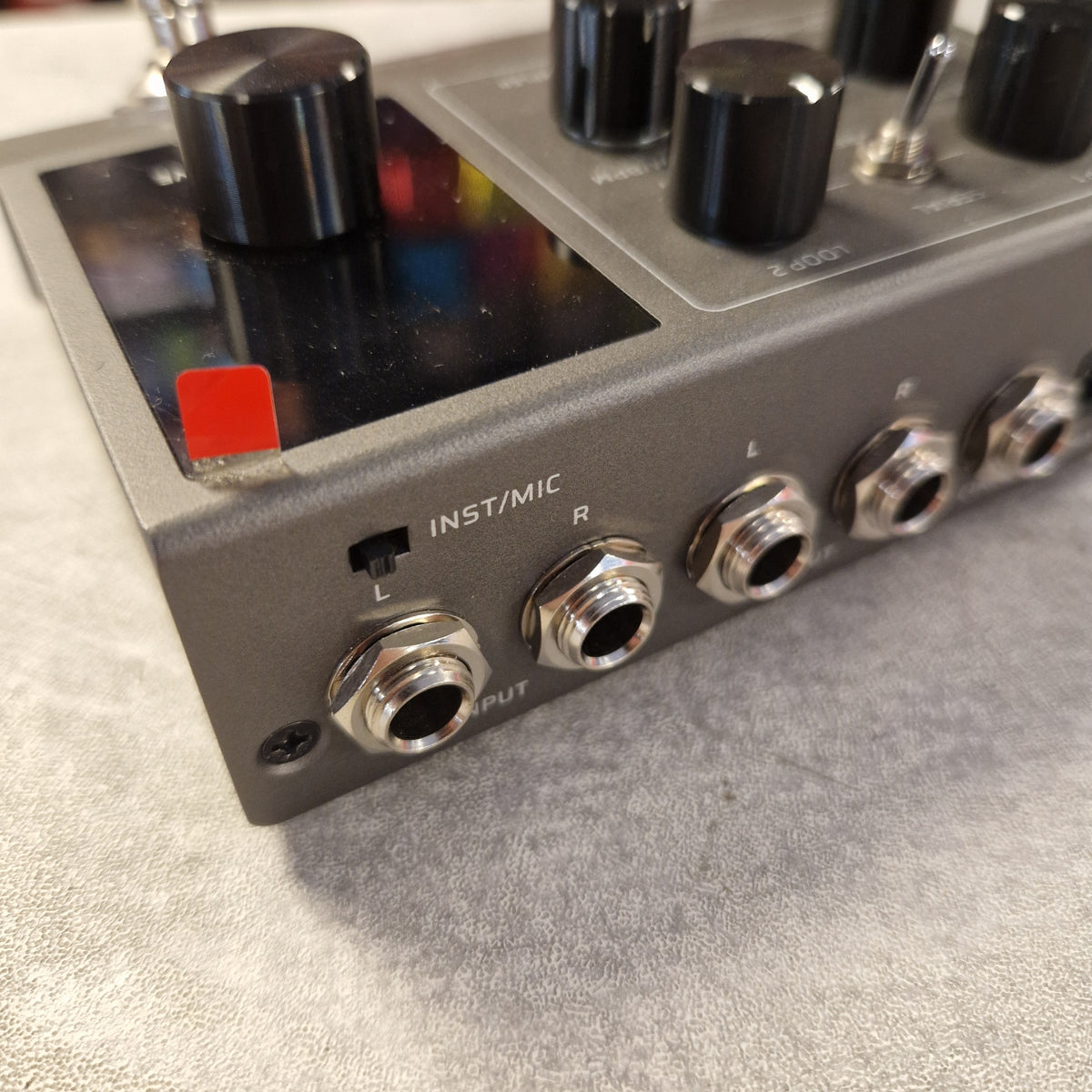 Pre-Owned Valeton VLP-200 Multi-Track Sampler w/ Box - Close-up of a gray electronic guitar effects pedal with black knobs, silver jacks, and a small red switch on a textured gray surface.