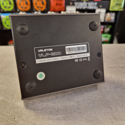 Pre-Owned Valeton VLP-200 Multi-Track Sampler w/ Box - A black Varleton VLP-200 9V 2A battery adapter shown from its back side, resting on a gray textured surface with a blurred store background.